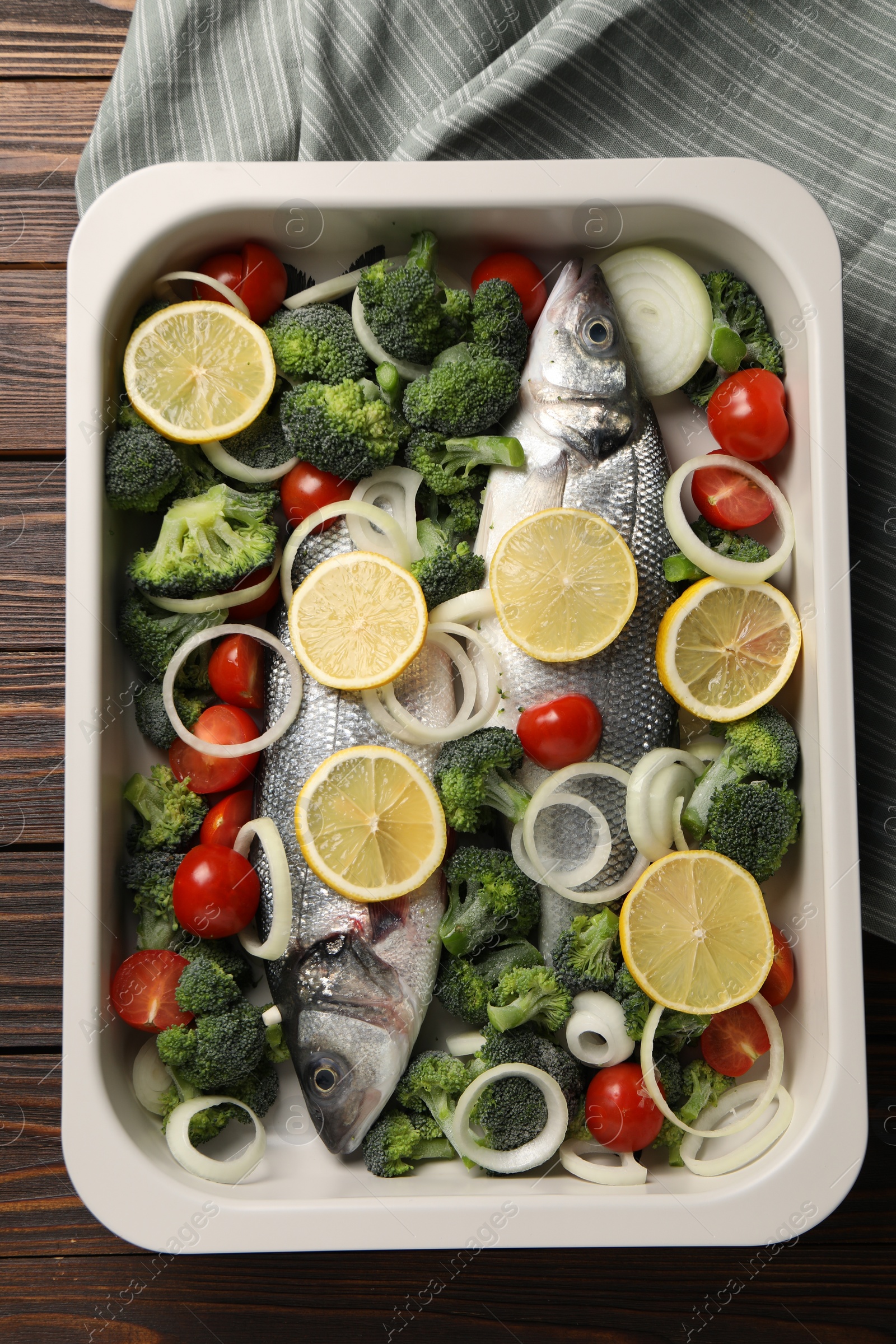 Photo of Raw fish with vegetables and lemon in baking dish on wooden table, top view