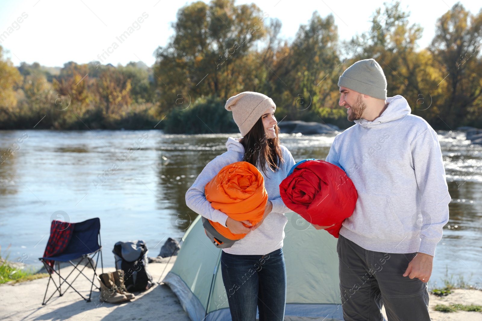 Photo of Young couple with sleeping bags near camping tent outdoors. Space for text