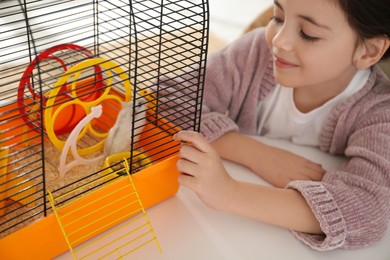 Little girl and her hamster in cage at home