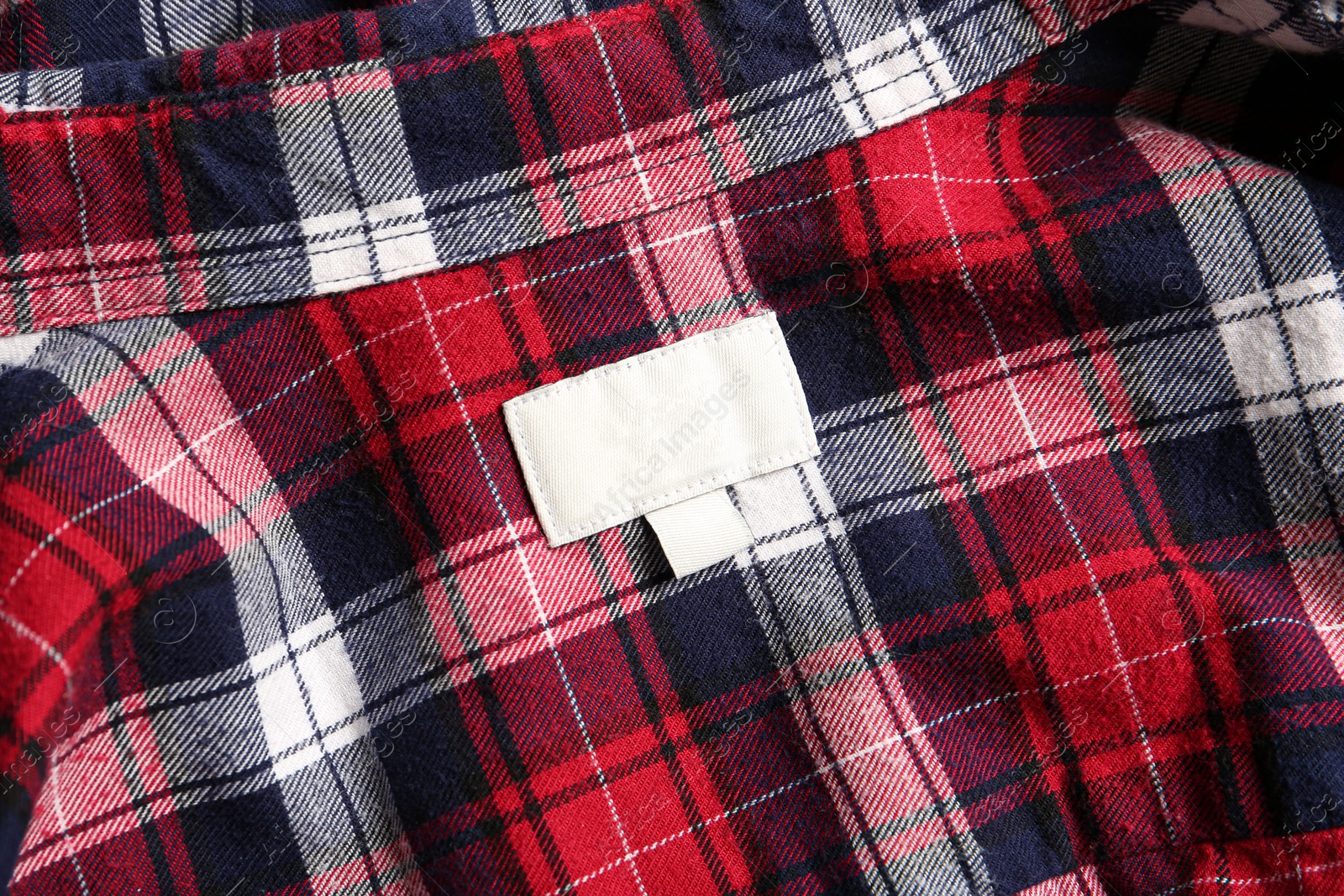 Photo of Blank clothing label on checkered shirt, top view