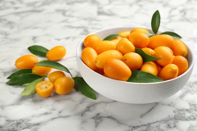 Fresh ripe kumquats in bowl on white marble table