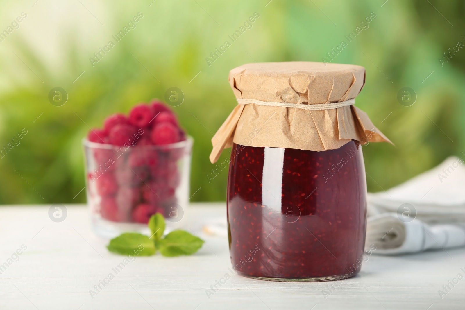 Photo of Jar with delicious raspberry jam on table against blurred background