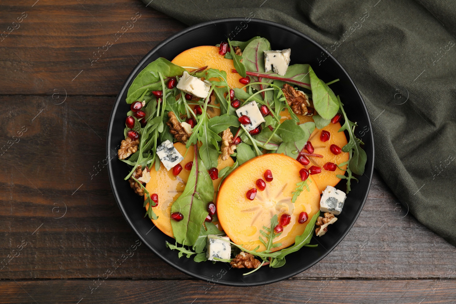 Photo of Tasty salad with persimmon, blue cheese, pomegranate and walnuts served on wooden table, top view