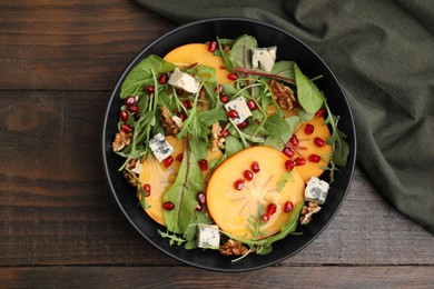 Tasty salad with persimmon, blue cheese, pomegranate and walnuts served on wooden table, top view