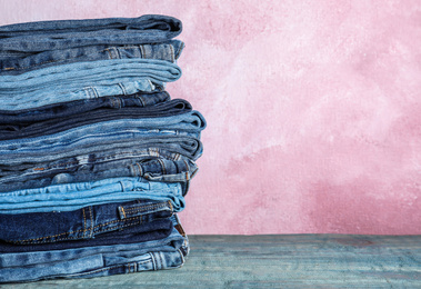 Stack of different jeans on blue wooden table against pink background. Space for text