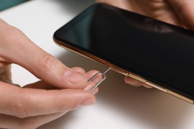 Woman with ejector opening SIM card tray in smartphone at white table, closeup