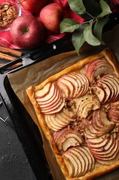 Photo of Baking tray with fresh apple galette and fruits on black textured table, flat lay