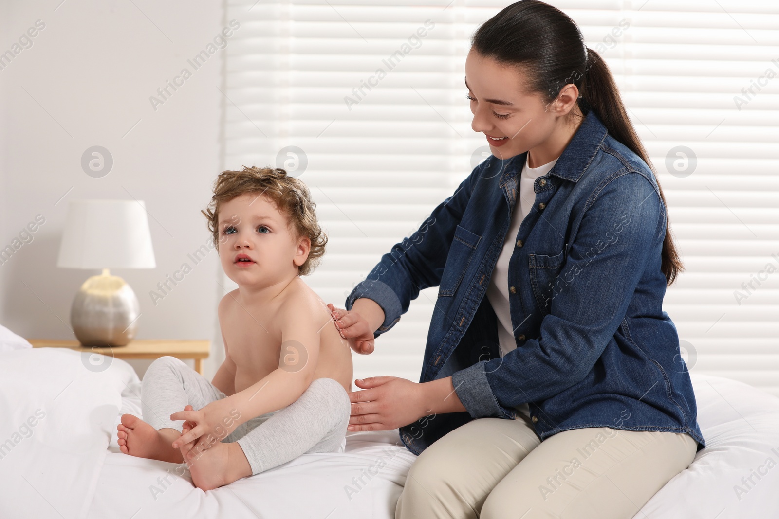 Photo of Mother applying ointment onto her son`s back on bed at home