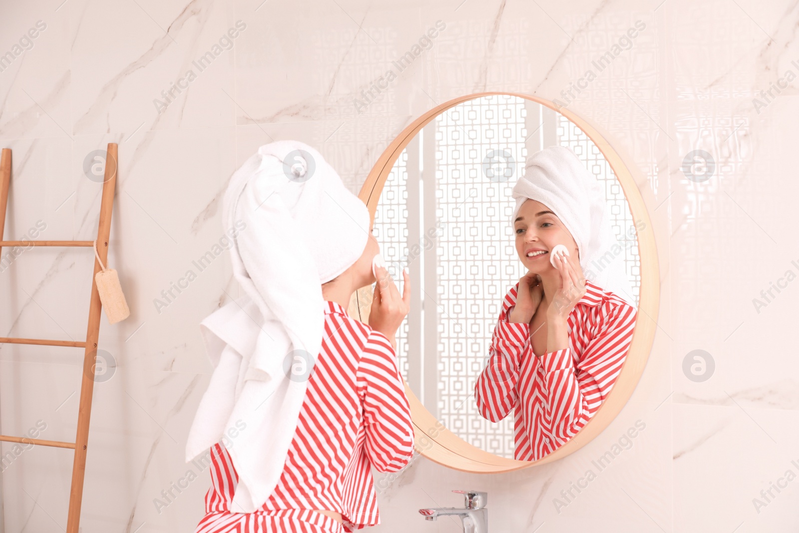 Photo of Young woman with towel on head near mirror in bathroom