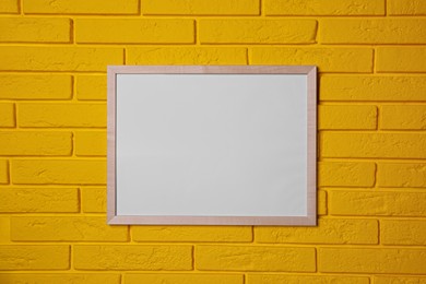 Photo of Empty frame on yellow brick wall. Mockup for design