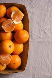 Photo of Paper box with fresh ripe tangerines on beige cloth, top view. Space for text