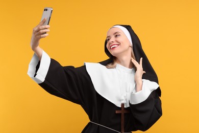 Happy woman in nun habit taking selfie against orange background