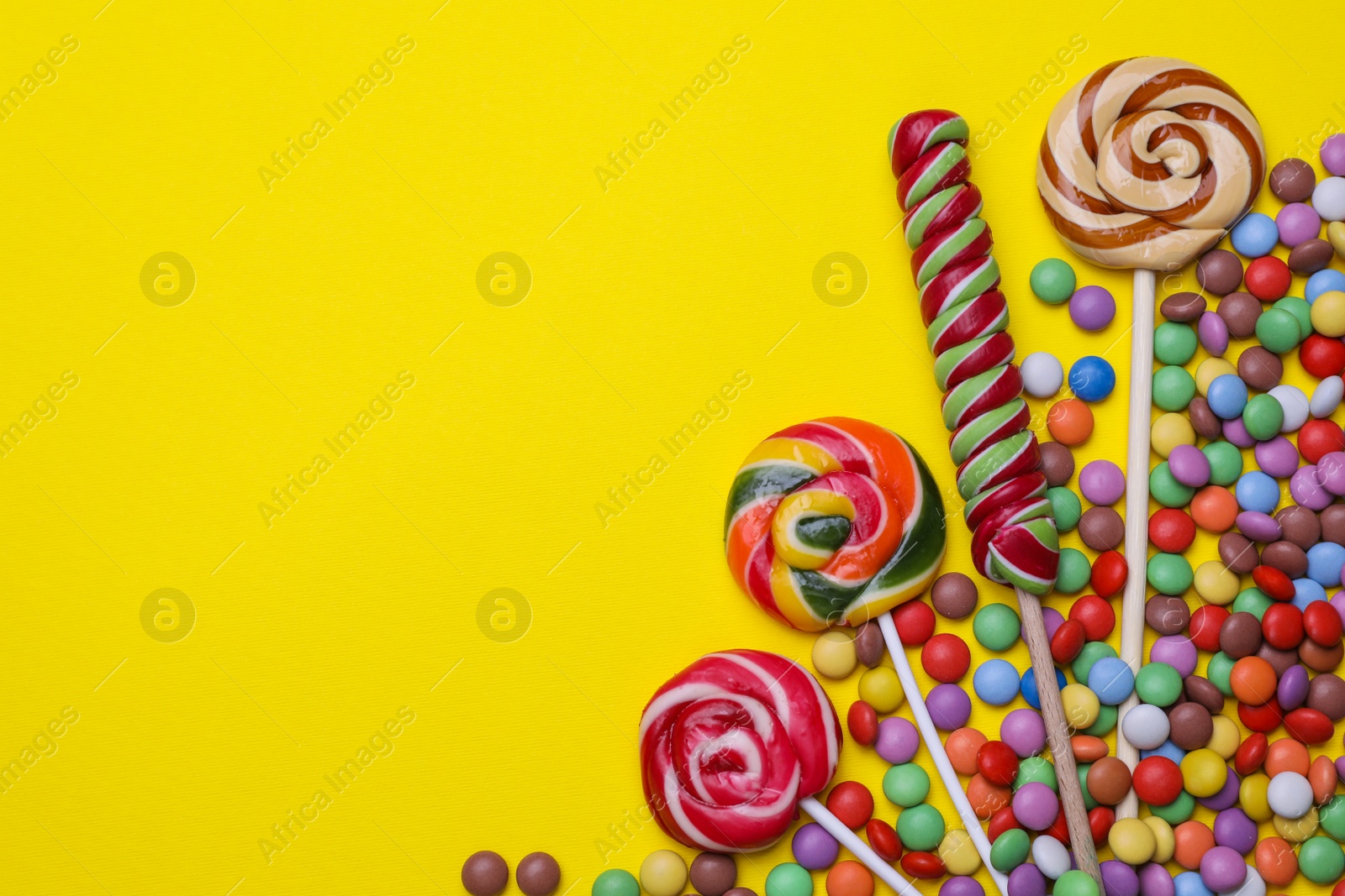 Photo of Delicious lollipops and candies on yellow background, flat lay. Space for text