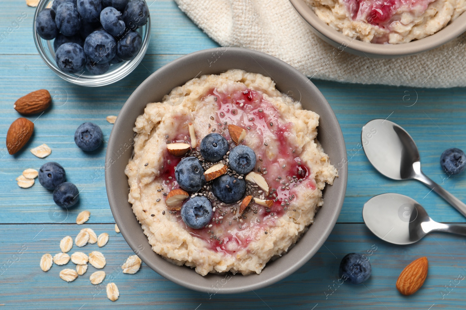 Photo of Tasty oatmeal porridge with toppings served on light blue wooden table, flat lay