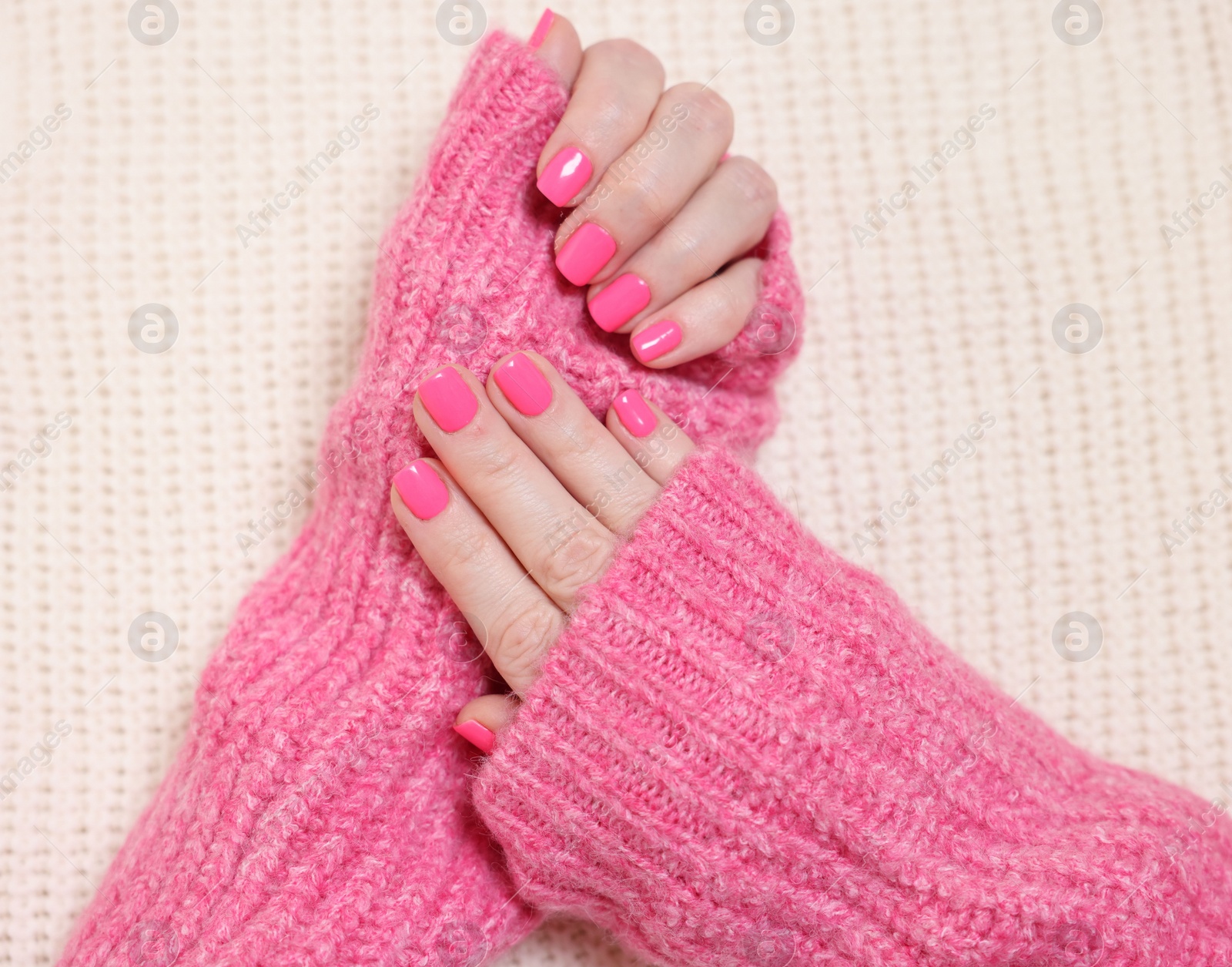 Photo of Woman showing her manicured hands with pink nail polish on knitted blanket, top view