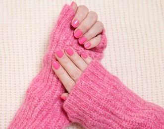 Photo of Woman showing her manicured hands with pink nail polish on knitted blanket, top view