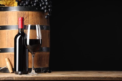 Delicious wine, wooden barrel and ripe grapes on table against black background. Space for text
