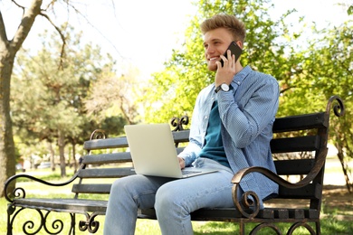 Happy young man with laptop talking on phone in park