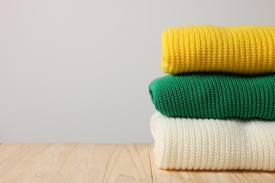 Photo of Stack of casual sweaters on wooden table against light background. Space for text