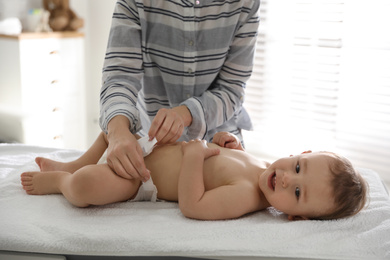 Mother changing baby's diaper on table at home