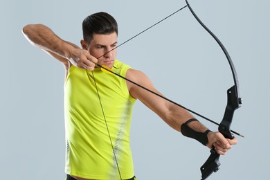 Photo of Man with bow and arrow practicing archery on light grey background