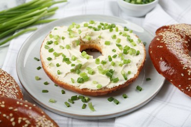 Delicious bagel with cream cheese and green onion on plate, closeup