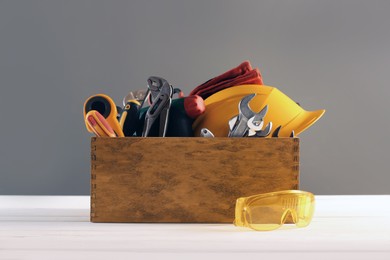 Wooden box with different tools for repair and protective glasses on white table