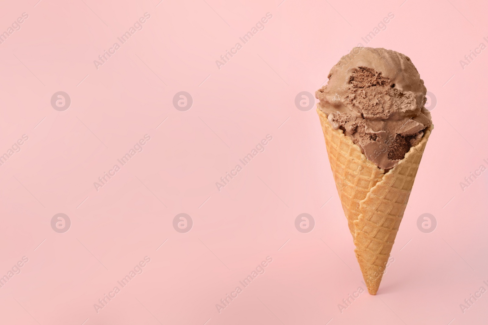 Photo of Delicious chocolate ice cream in waffle cone on pink background. Space for text