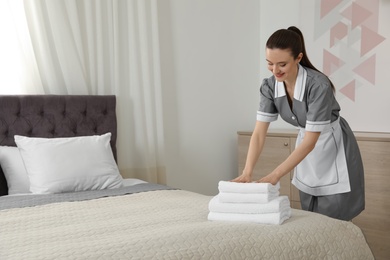 Photo of Chambermaid putting fresh towels on bed in hotel room. Space for text