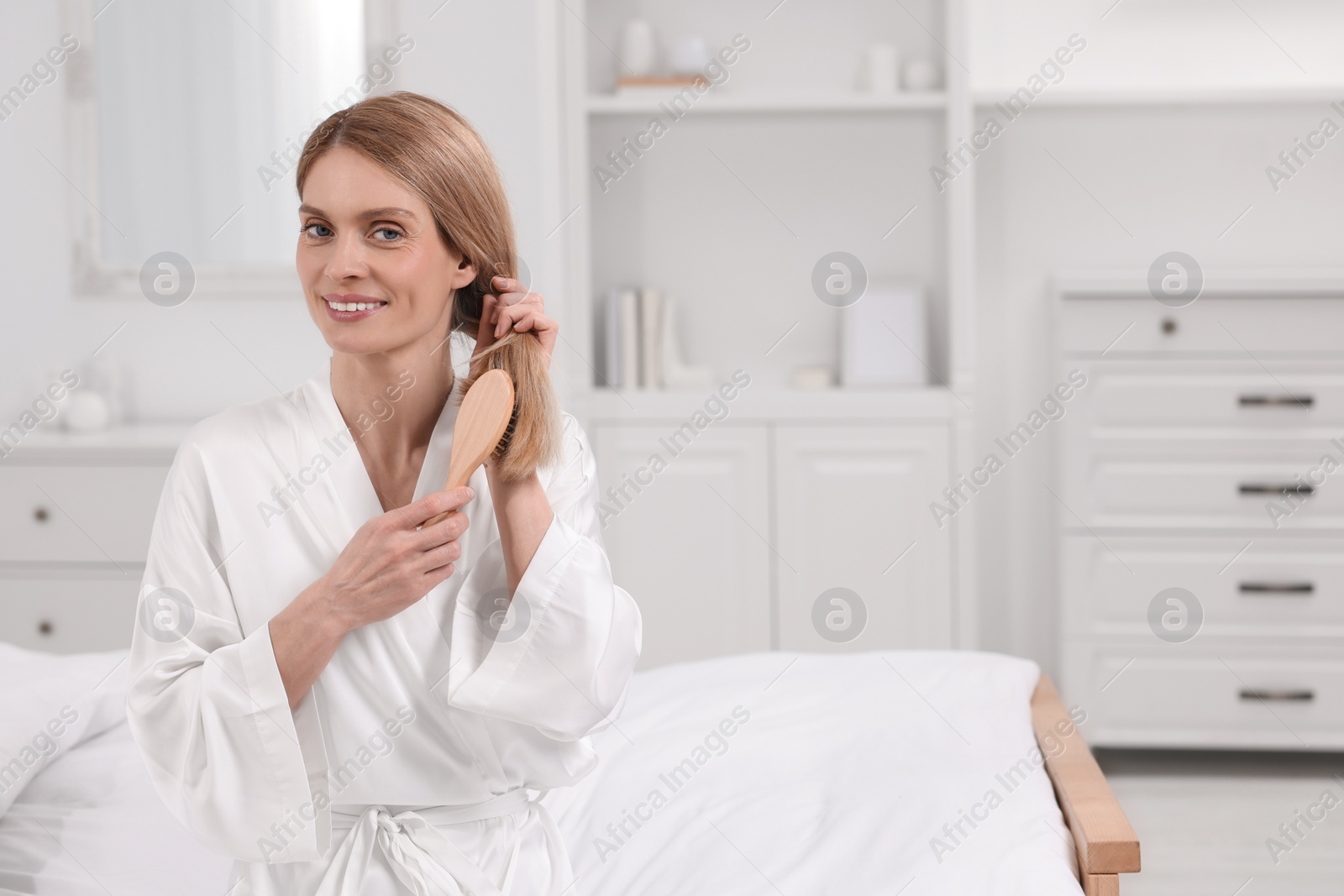 Photo of Beautiful woman brushing her hair on bed in room