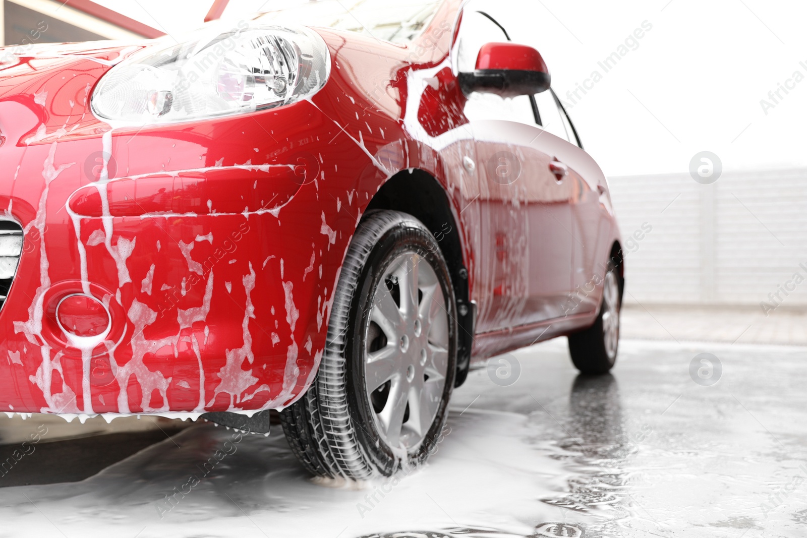 Photo of Red auto with foam at car wash. Cleaning service