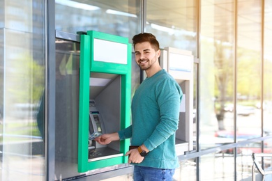 Young man taking money from cash machine outdoors