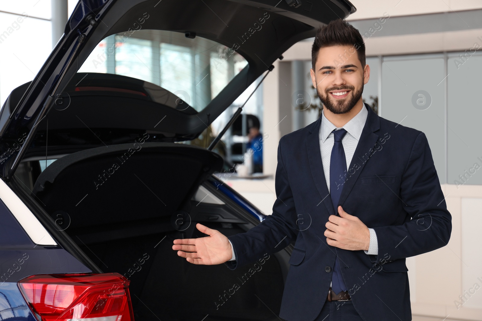 Photo of Young salesman near new car in dealership