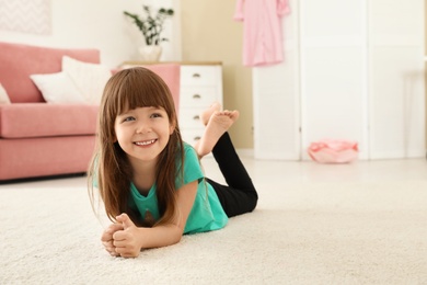 Photo of Cute little girl lying on carpet at home. Space for text