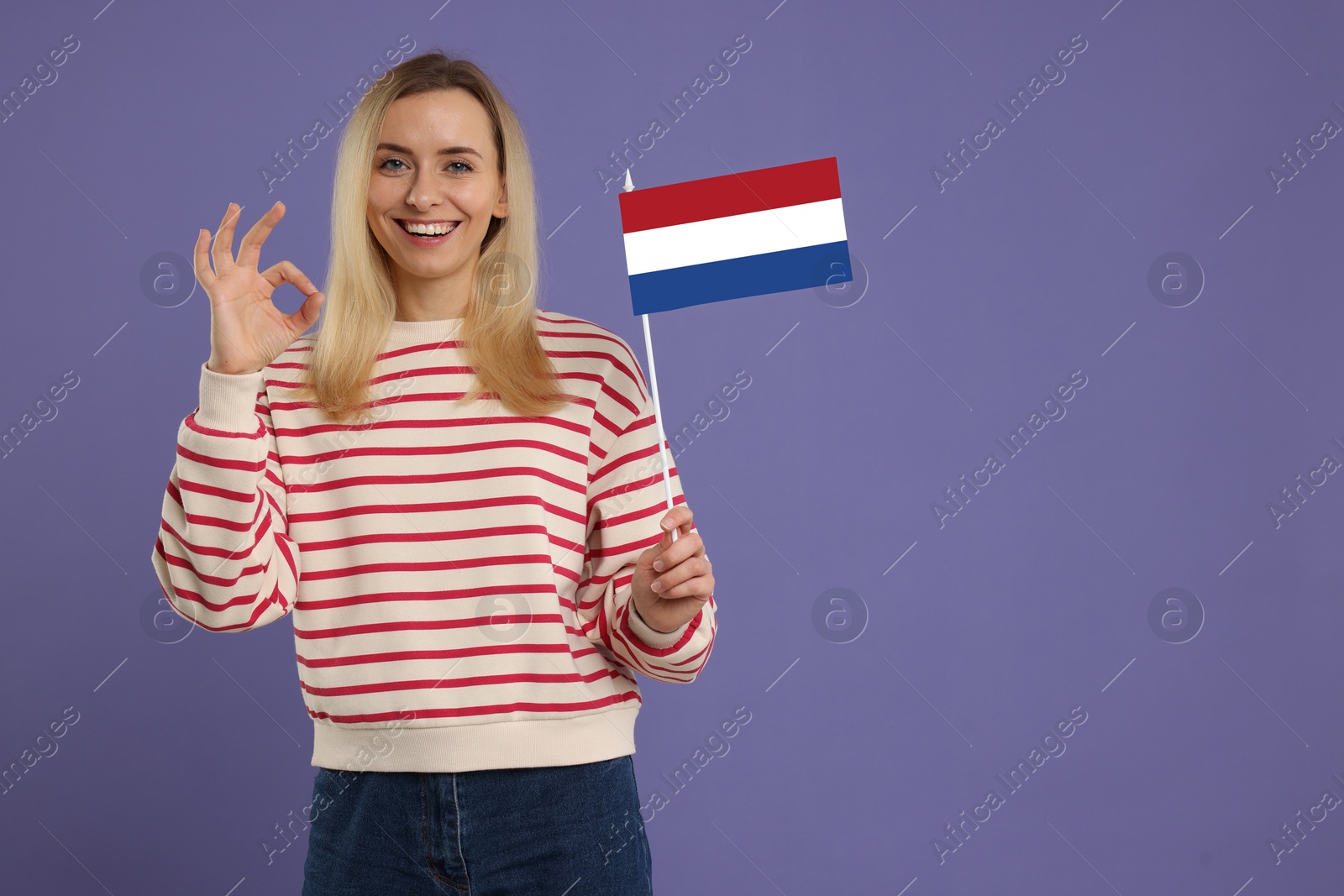 Image of Happy young woman with flag of France showing OK gesture on purple background