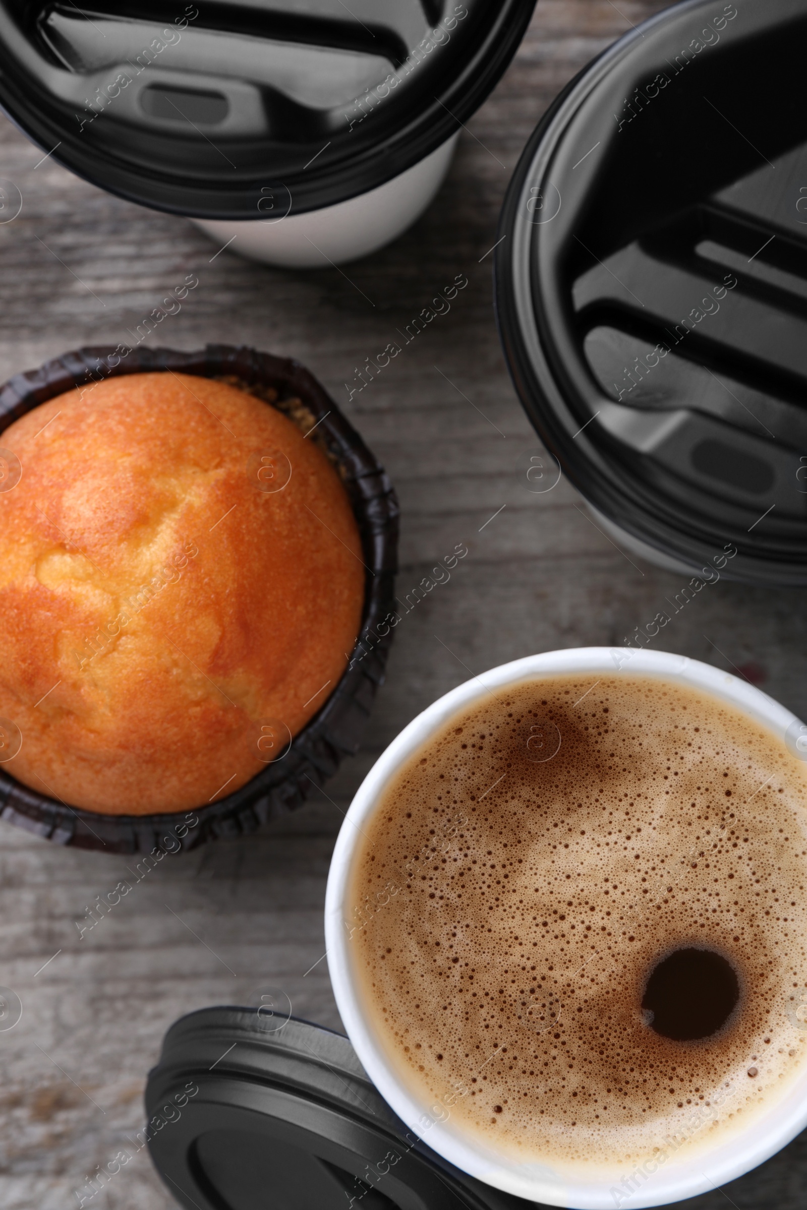 Photo of Coffee to go. Paper cups with tasty drink and muffin on wooden table, flat lay