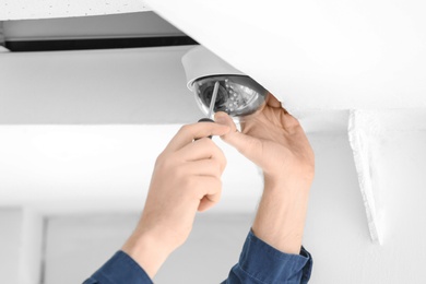 Technician installing CCTV camera on ceiling indoors, closeup