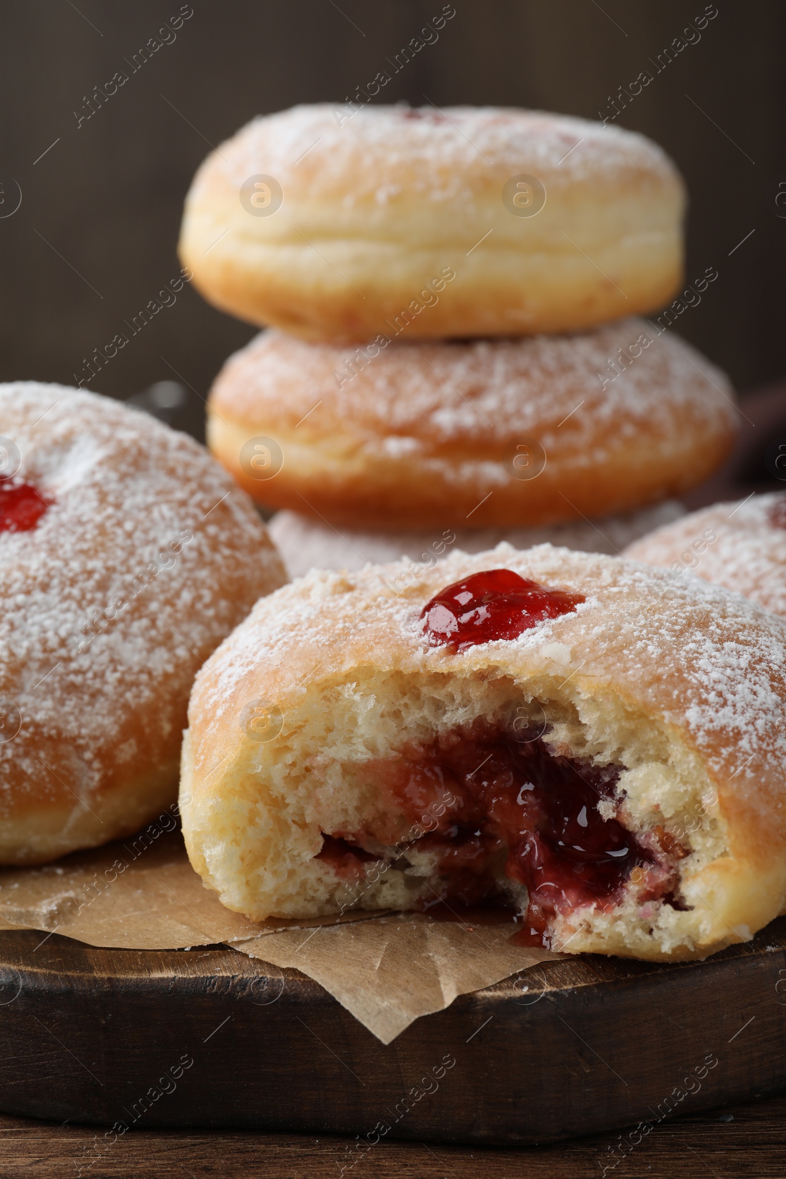 Photo of Delicious donuts with jelly and powdered sugar on wooden board, closeup