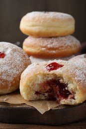 Delicious donuts with jelly and powdered sugar on wooden board, closeup