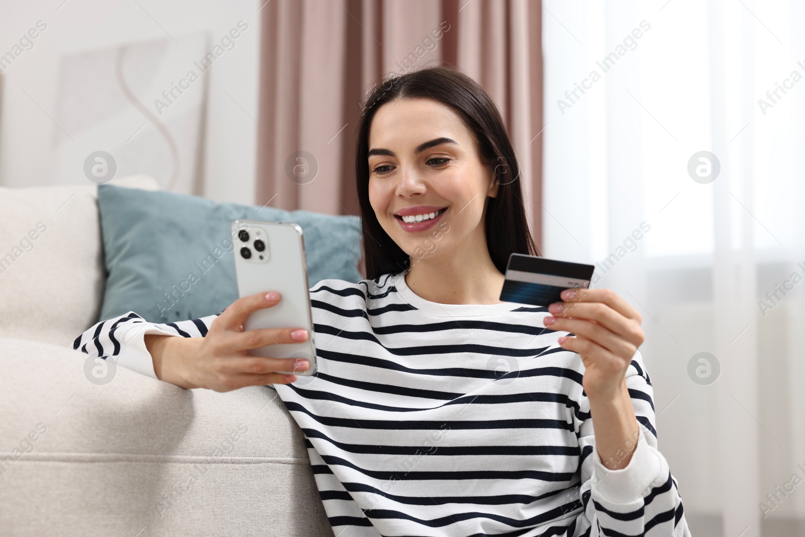 Photo of Happy young woman with credit card using smartphone for shopping online at home