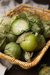 Photo of Fresh green tomatillos with husk in wicker basket on table, closeup