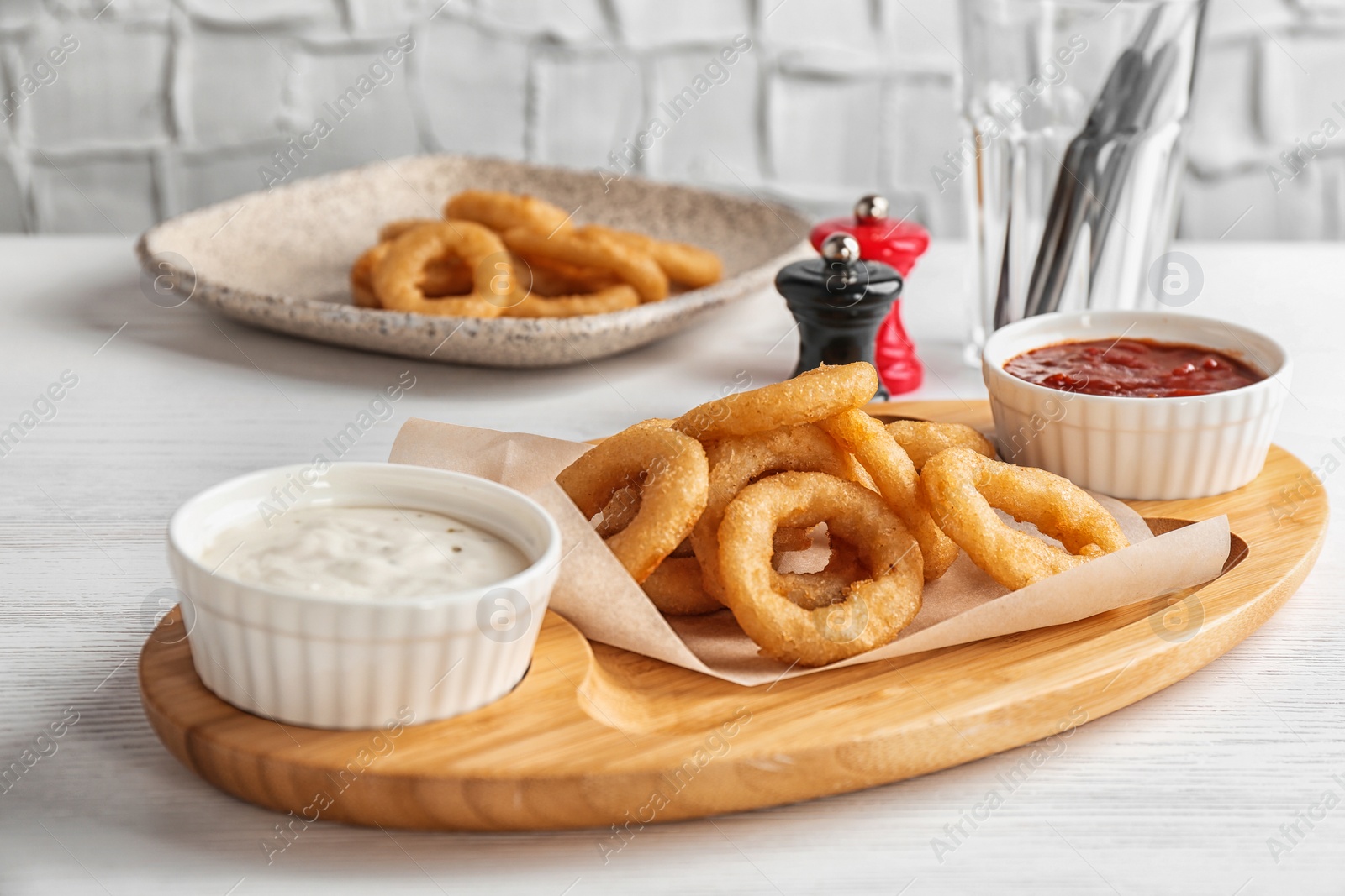 Photo of Wooden board with tasty onion rings and sauces on table