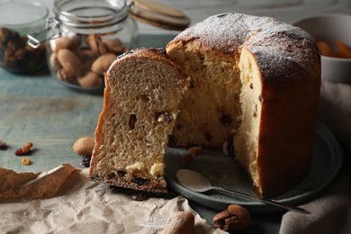 Photo of Delicious cut Panettone cake with powdered sugar and raisins on light blue wooden table. Traditional Italian pastry