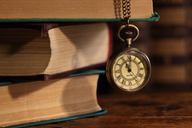 Pocket clock hanging on stack of books at wooden table, closeup