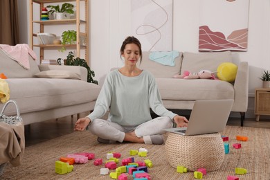 Photo of Young mother meditating on floor in messy living room