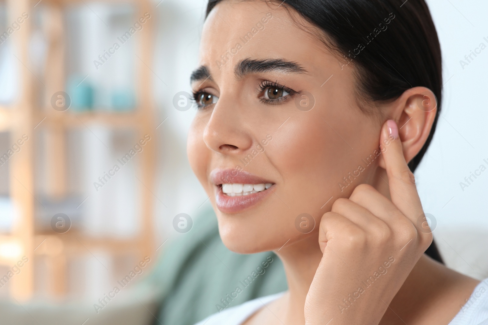 Photo of Young woman suffering from ear pain indoors, closeup