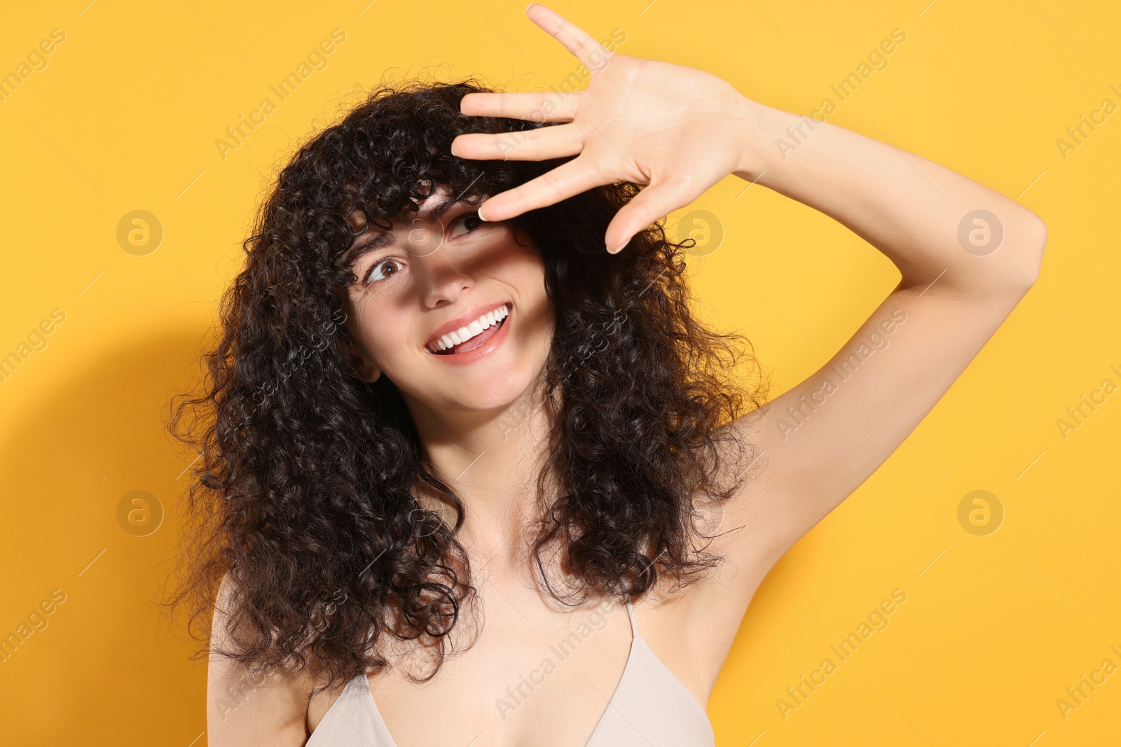 Photo of Beautiful young woman shading herself with hand from sunlight against orange background