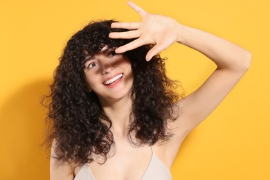 Beautiful young woman shading herself with hand from sunlight against orange background
