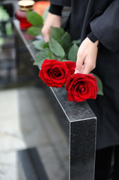 Woman with red roses near black granite tombstone outdoors, closeup. Funeral ceremony