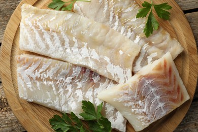Photo of Fresh raw cod fillets and parsley on wooden table, top view